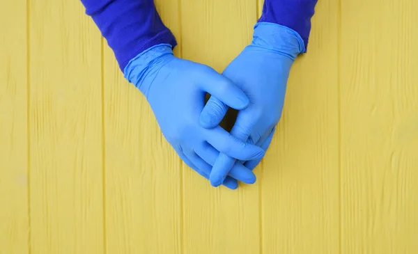 Blue gloved hands close up on yellow wooden background. Call for hand disinfection. Stop coronavirus concept. Using antibacterial gel for hands during quarantine lockdown — Stock Photo, Image