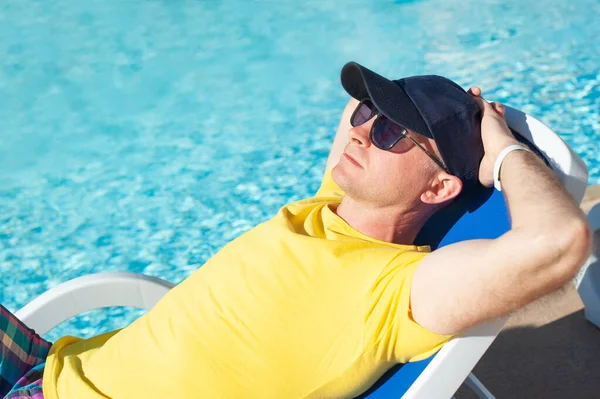 Hombre joven y exitoso tumbado en una tumbona en el hotel cerca de la piscina. Relájese en la piscina de verano. Concepto de tiempo para viajar en verano — Foto de Stock