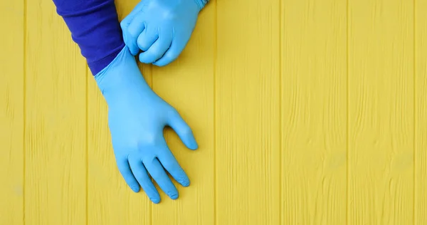 Banner blue Nitrile gloves. Hands of a medic in the blue latex gloves on a yellow wooden background with place for your text