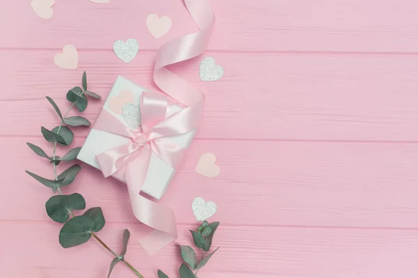 Día de San Valentín o regalo de boda, hojas de eucalipto marco corazones de papel confeti y fondo rosa de madera, espacio vacío para su texto, vista superior plano laico — Foto de Stock