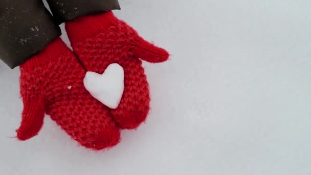 Manos femeninas en manoplas rojas con corazón nevado sobre fondo de nieve. Concepto de San Valentín — Vídeos de Stock