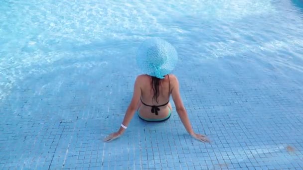 Mavi şapkalı mutlu genç bayan oteldeki havuzda oturuyor. Mısır 'da gerçek dinlenme. Denizde tatil köyü. Video ProRes 1920x1080 — Stok video