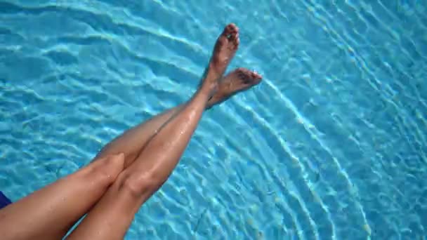 炎炎夏日,纤细的女性腿在游泳池里飞溅.在阳光灿烂的日子里，比基尼女孩在游泳池里放松，用脚泼水。顶部视图 — 图库视频影像