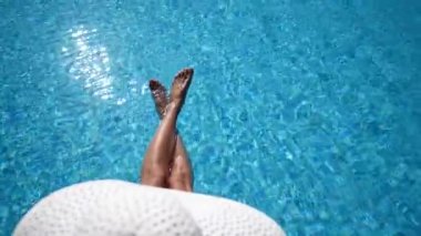 Sıcak bir yaz gününde sıska kadın bacakları havuza düşer ve büyük beyaz bir şapka takar. Bikinili kız güneşli bir günde yüzme havuzunda dinleniyor, suya ayaklarıyla su sıçratıyor. Üst görünüm