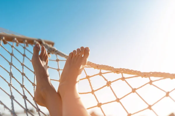 View of woman relaxing on hammock. Low angle view. Beautiful female feet relaxing in a hammock on the beach against the background of the sky. horizontal is place for your text — Stock Photo, Image