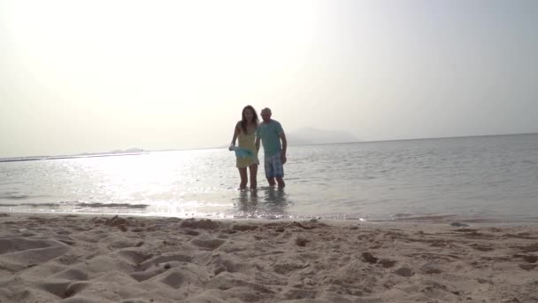 Romantyczna para biegająca po plaży o zachodzie słońca trzymająca się za ręce. Pojęcie miłości i szczęścia — Wideo stockowe