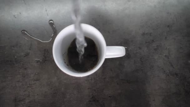 Pouring hot water in slow motion on grounded coffee crystals in a white ceramic cup and brewing instant coffee drink for a morning energy shot or for a working day break — Stock Video