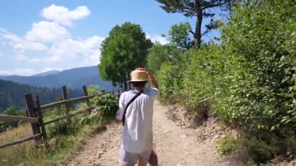 Νεαρή όμορφη Ευρωπαία γυναίκα με σκούρα μαλλιά σε ψάθινο καπέλο πηγαίνει στο δρόμο του χωριού. πίσω όψη. Βίντεο βίντεο Full HD — Αρχείο Βίντεο