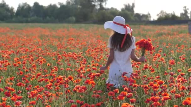 Молода брюнетка в білій сукні стоїть посеред поля маків. Чарівна леді з неймовірною посмішкою з букетом маків в руках. Повільний рух Full HD — стокове відео