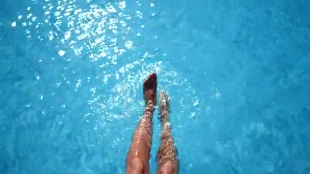 Delgadas piernas femeninas chapotean en la piscina en un caluroso día de verano. Chica bikini relajante en la piscina en un día soleado, salpicando agua con los pies. Vista superior — Vídeos de Stock