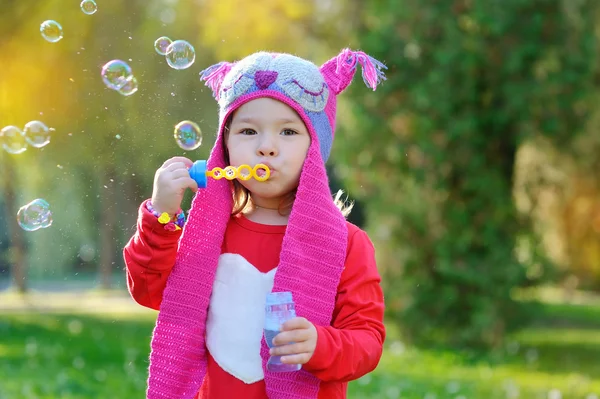 Menina com bolhas de sabão em um chapéu de malha feito à mão — Fotografia de Stock