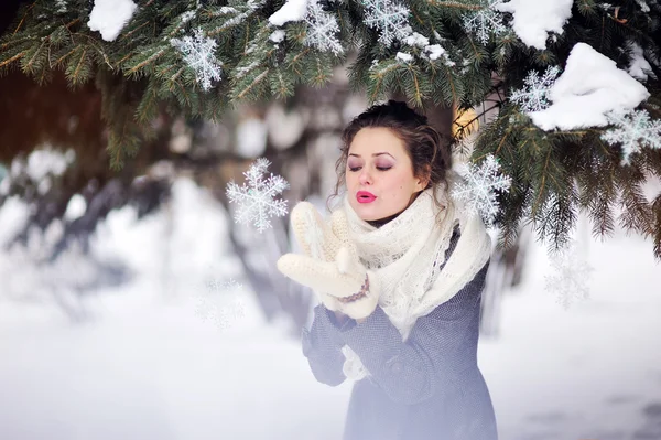 Зимняя девушка, дующая на снежинку в вязаных варежках — стоковое фото