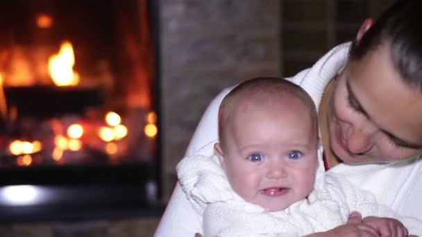 Madre sentada con su bebé cerca de la chimenea en Navidad — Vídeos de Stock
