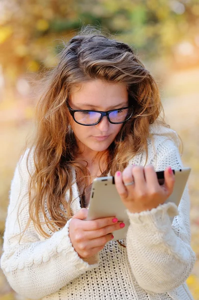 Girl in glasses with a tablet in hands in park — Stock Photo, Image