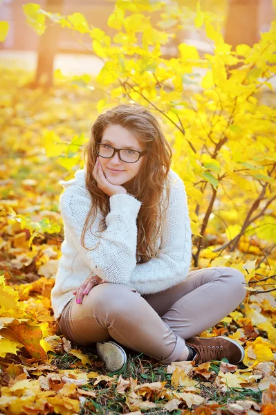 Mädchen mit Brille sitzt im Herbstpark auf Blättern — Stockfoto