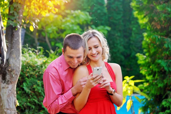 Jovem casal brincando com telefone inteligente no parque — Fotografia de Stock