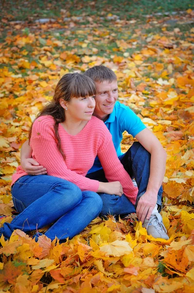 Pareja enamorada sentada en las hojas de otoño — Foto de Stock