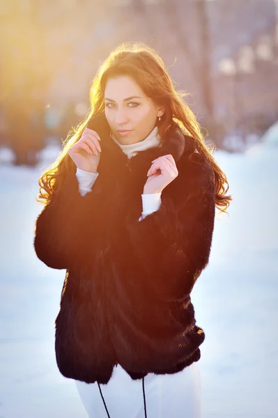 Belle fille en manteau de fourrure d'hiver. Coucher de soleil rétroéclairé soleil — Photo