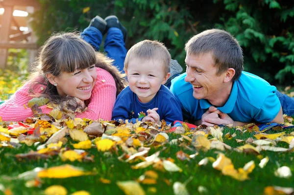 Padre, madre e hijo feliz familia en un césped verde en el otoño —  Fotos de Stock