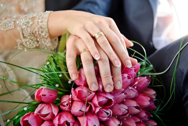 Mãos com anéis noiva e noivo no buquê de casamento de rosa — Fotografia de Stock