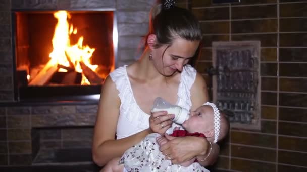 Moeder voedt haar baby met een fles in de buurt van een open haard — Stockvideo