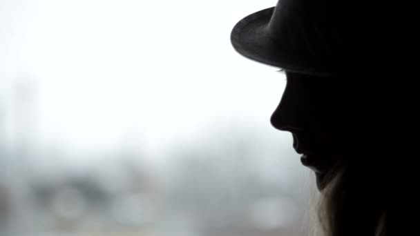 Silhuetten av en vacker flicka i en hatt mot fönstret — Stockvideo