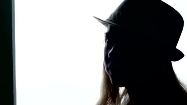 Silhouette of a beautiful girl in a hat against the window — Stock Video