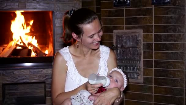 Мать кормит ребенка из бутылки у огня — стоковое видео