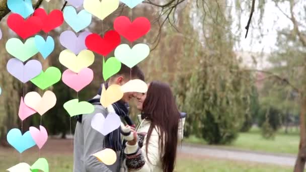 Любляча пара стоїть біля різнокольорових сердець — стокове відео