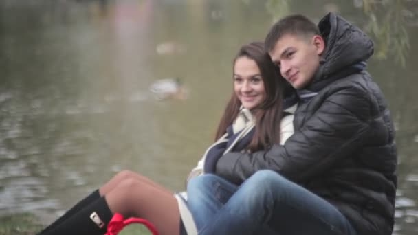 Любляча пара обіймає сидячи біля озера — стокове відео