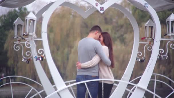 Älskande par stående i lusthuset i form av hjärta i parken — Stockvideo