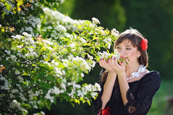 Bela mulher está cheirando flores brancas no parque da primavera — Fotografia de Stock