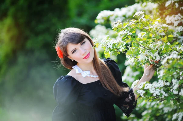 Hermosa chica con un lazo rojo en el parque de flores de primavera —  Fotos de Stock