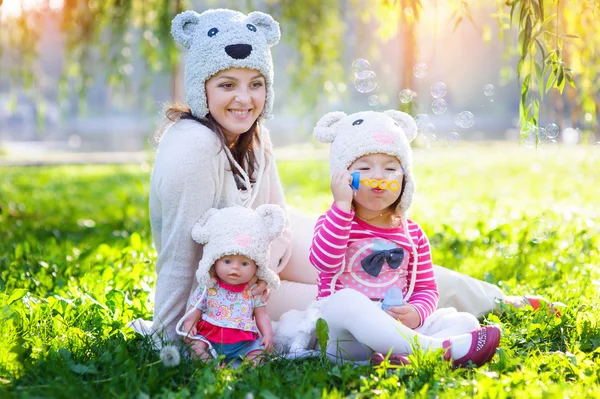 Mamá y su hija jugando en el parque con una muñeca en gorras — Foto de Stock