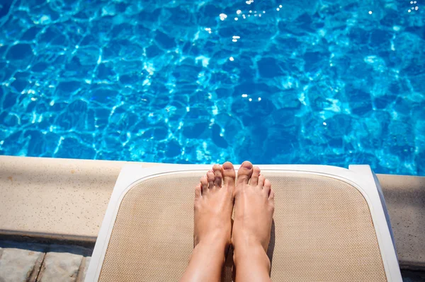 Gambe femminili su un lettino sullo sfondo della piscina — Foto Stock