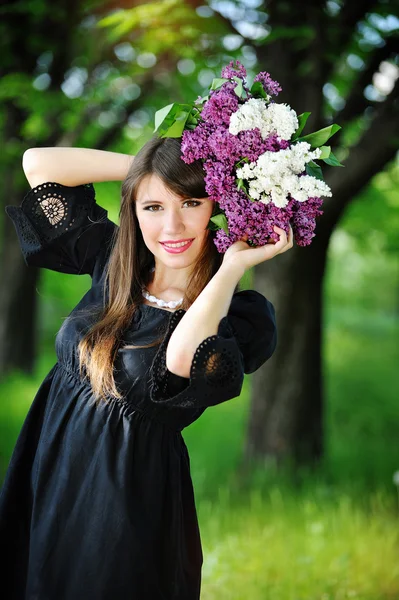 Giovane donna in un parco primaverile con lilla — Foto Stock