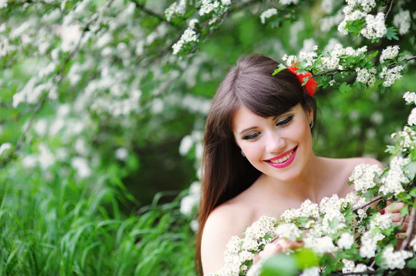 Gelukkig jonge vrouw in een park van de lente de bloemen ruiken — Stockfoto