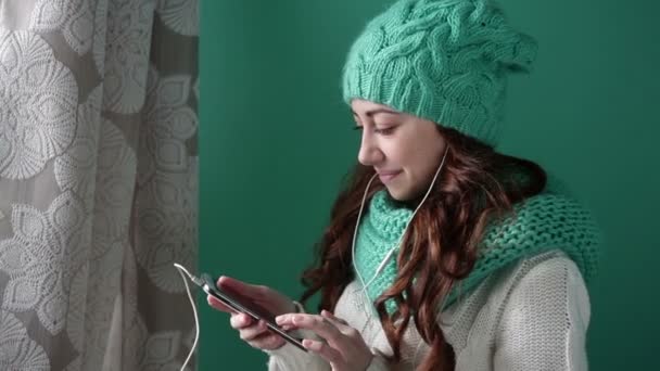 Menina bonita em um chapéu de malha turquesa ouvindo música — Vídeo de Stock