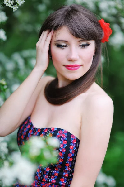 Menina bonita com flor vermelha na cabeça no jardim da primavera — Fotografia de Stock