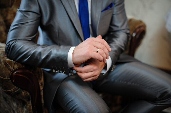 man in a suit sitting in a chair and puts cufflinks