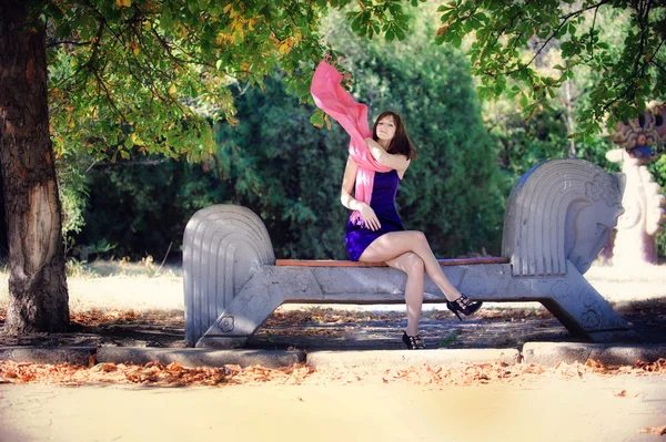 Mooie vrouw in een blauwe jurk zittend op een bankje in het park — Stockfoto