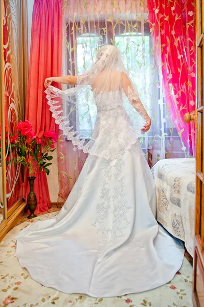 Bride in white dress in the room looking out the window and keep — Stock Photo, Image