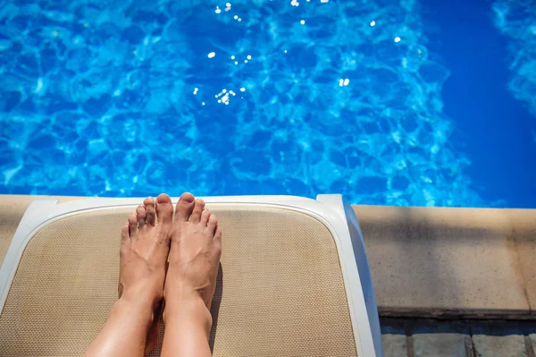 Chicas piernas bronceadas primer plano en una tumbona junto a la piscina — Foto de Stock