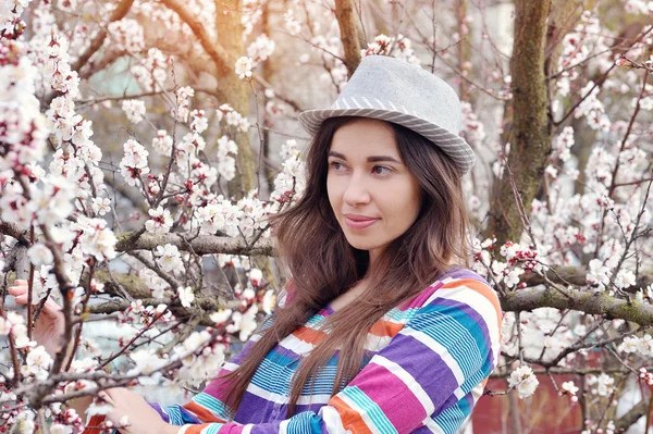 Mulher bonita em um chapéu no jardim de primavera florescente — Fotografia de Stock