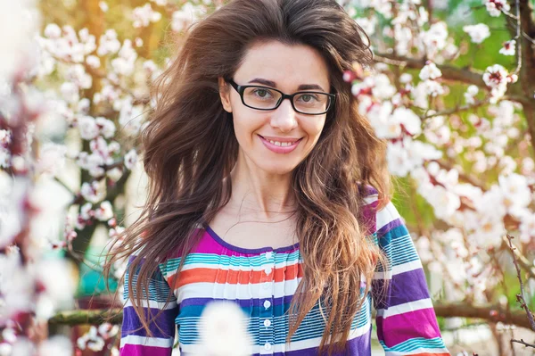 Morena en gafas sobre un fondo de un árbol en flor en spri —  Fotos de Stock