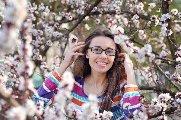Morena en gafas sobre un fondo de un árbol en flor en spri —  Fotos de Stock
