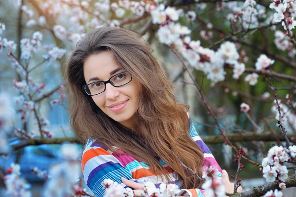 Brunetka w okularach na tle drzew kwitnących w spri — Zdjęcie stockowe