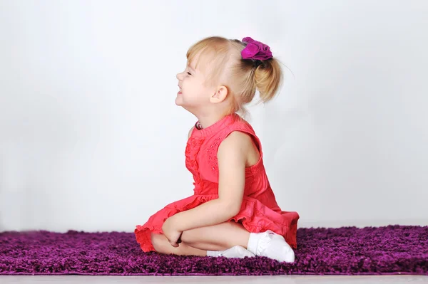 Kleines lachendes Mädchen sitzt auf lila Teppich im Studio — Stockfoto