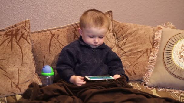 Niño sentado en el sofá y viendo una caricatura en su teléfono inteligente — Vídeo de stock