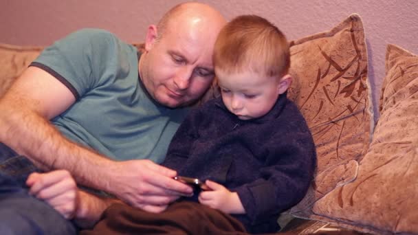 Kleine jongen met zijn oom lettend op een film op uw telefoon — Stockvideo